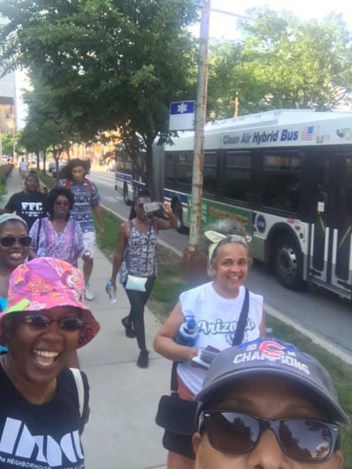 A group selfie of smiling neighbors walking along a South Shore sidewalk beside a CTA bus